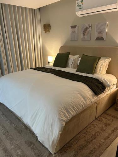 a large bed with white sheets and green pillows at Malath - The Bohemian Haven in Dammam