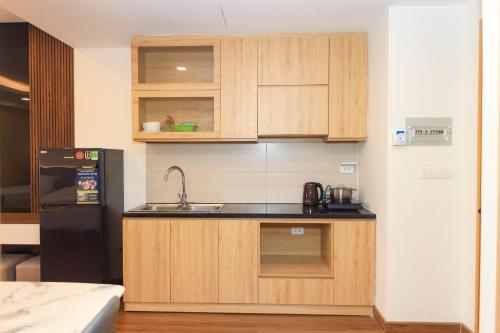 a kitchen with wooden cabinets and a black refrigerator at FLC Sea Tower Quy Nhơn Seaview Apartment in Quy Nhon