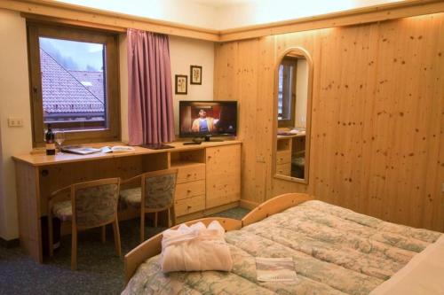 a bedroom with a bed and a desk and a television at Hotel Alpi in Campitello di Fassa