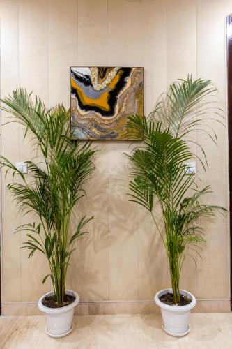 two palm trees in pots in a room with a painting at Aliste Millennium Huda City Centre in Gurgaon