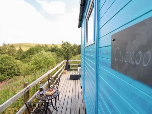 a blue building with a table and chairs on a deck at Cuckoo at Wild Valley Huts in Oswestry