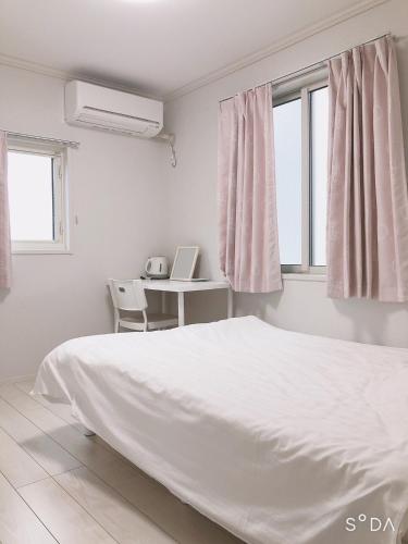 a white bedroom with a bed and a desk and windows at Putao in Osaka