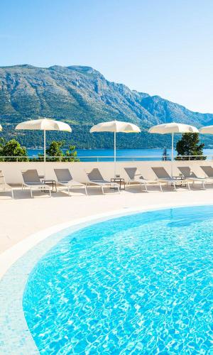 a swimming pool with chairs and umbrellas at Marko Polo Maradiso Hotel by Aminess in Korčula