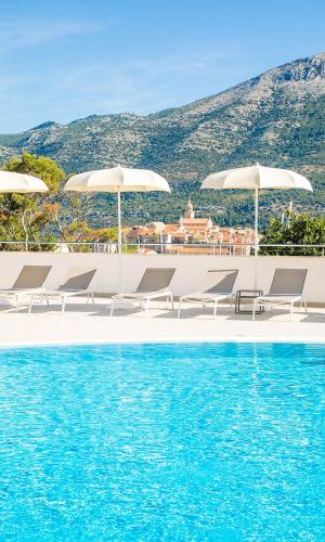 a pool with chairs and umbrellas next to the water at Marko Polo Maradiso Hotel by Aminess in Korčula