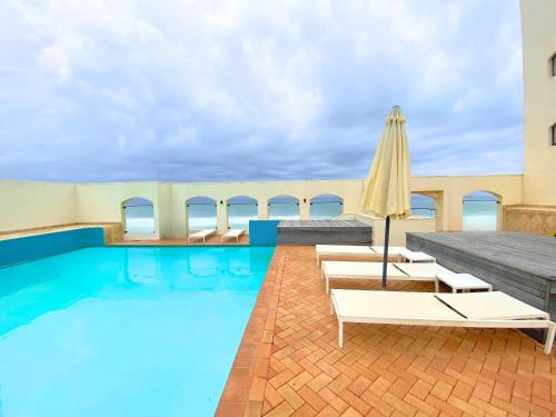 a swimming pool with chairs and an umbrella at 1001 Bermudas - Seaviews & beach access - Modern 3BR Umhlanga in Durban