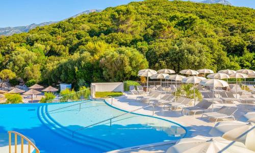 a swimming pool with chairs and umbrellas and a mountain at Aminess Vival Port9 Residence in Korčula