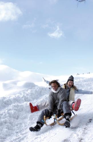 two people are sitting in the snow on a sled at Hotel Oberwirt - nahe an Saalbach und Zell am See, Viehhofen Sommercard in Viehhofen