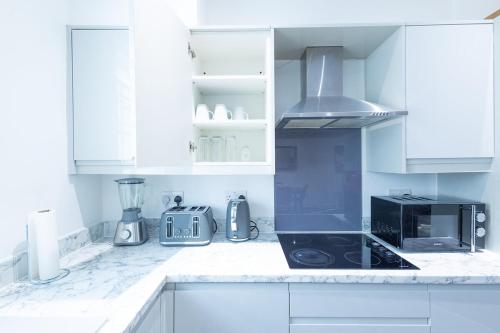 a kitchen with white cabinets and a black stove top oven at Cozy Riverside Apartment 5mins to train station in Gravesend