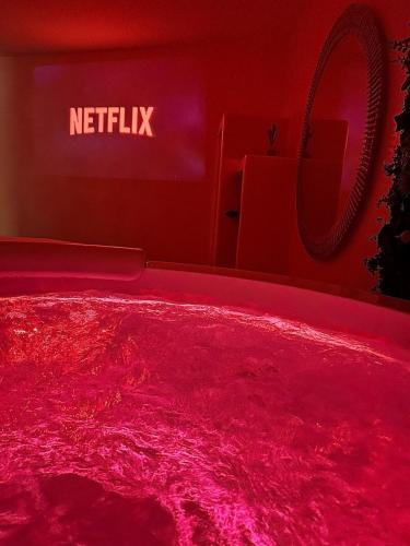 a red bed in a room with a netflix sign at Suite Myria, Balnéo & Cinéma - 1 heure de Paris in Maintenon