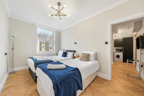two beds in a room with white walls and wood floors at Cambridge Court Central Flats in London