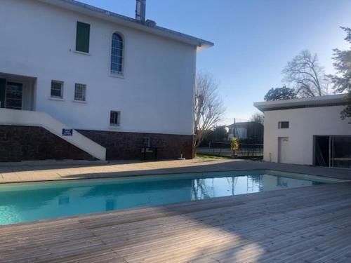 a swimming pool in front of a white house at L'écrin vert - proche gare, piscine , tennis, wifi in Labouheyre