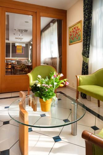 a living room with a glass table and two green chairs at Hotel Kálvária in Győr