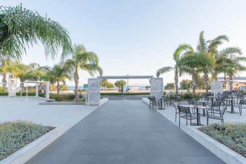 a patio with tables and chairs and palm trees at Belair Beach Hotel in Ixia