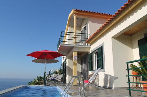 a house with a pool and a red umbrella at OurMadeira - Casa Jardim Mar, seaviews in Ponta do Sol