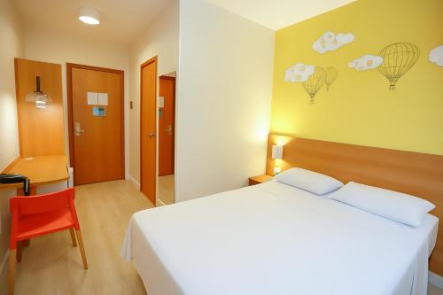 a bedroom with a white bed and a red chair at Hotel Dan Inn São Carlos By Nacional Inn in São Carlos