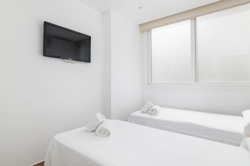 a white room with two beds and a tv on the wall at Apartamentos Almadraba in Zahara de los Atunes