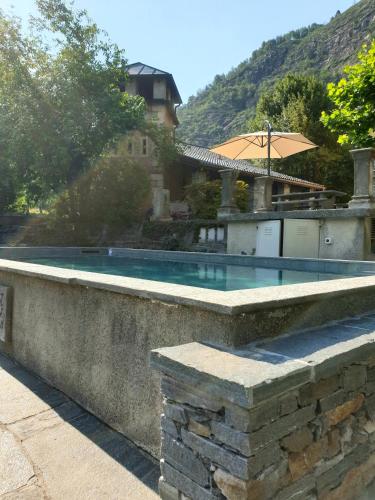a swimming pool in a stone wall with an umbrella at Villa Corfù in Ponte Brolla