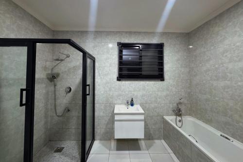 ルサカにあるNiza Homes, Luxury Kalundu Escapeのシャワー、洗面台、浴槽を備えたバスルーム