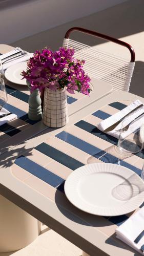 a table with white plates and purple flowers in a vase at Neema Maison Finikia Santorini in Oia