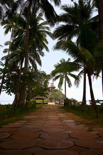 a road with palm trees and a building in the distance at Sangat Island Dive Resort in Coron
