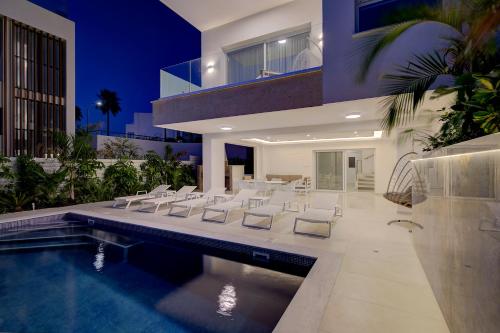 a house with a pool with white chairs and a swimming pool at Olymp White Palace - The Ultra Luxury Beach House in Kissonerga