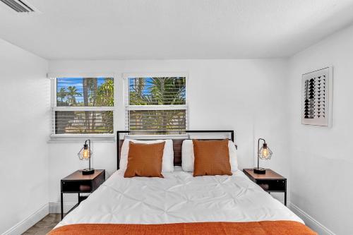 ein Schlafzimmer mit einem Bett mit zwei Nachttischen und zwei Fenstern in der Unterkunft Private Jungle Pool Home - Arcade Games & Pool in Fort Lauderdale