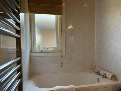 Una bañera blanca en un baño con ventana. en Oakwood 1, en Rousdon