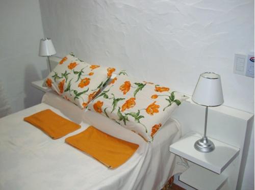 Cama blanca con almohadas naranjas y mesa con lámpara en Cabañas Calma Chicha en Cortaderas