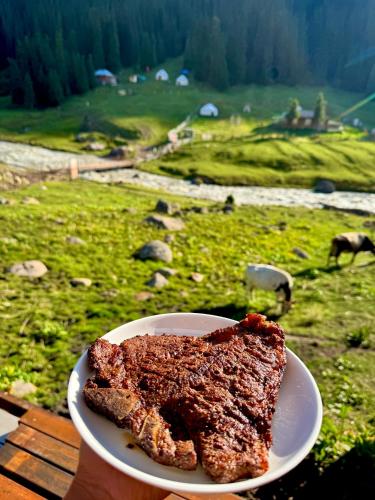 a person holding a plate of meat on a table at Arashan Hotel in Mineralʼnyy Istochnik Altyn-Arasan