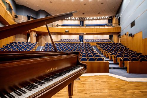 a piano in a lecture hall with blue chairs at Notre Dame of Jerusalem Center in Jerusalem