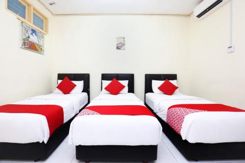 three beds in a room with white walls and red pillows at Hotel O Pelangi Marang in Marang