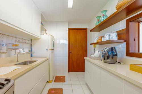 Una cocina blanca con fregadero y refrigerador. en PF112 Magnífico apartamento frente al mar con 2 suites - Praia do Forte, en Praia do Forte