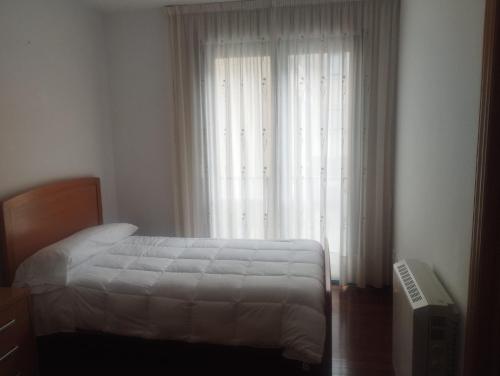 a bedroom with a bed and a window with white curtains at Piso Ría de Ribadeo in Ribadeo