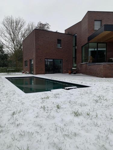 a swimming pool in front of a brick building at Villa Tussenin in Gistel