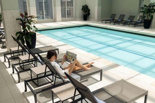 a woman sitting in a chair reading a book next to a swimming pool at Palace Hotel, a Luxury Collection Hotel, San Francisco in San Francisco