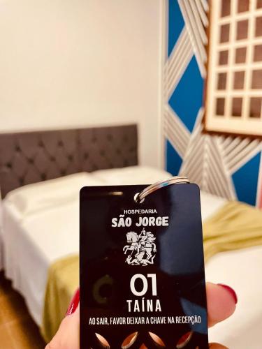 a person holding a cell phone in front of a bed at Hospedaria São Jorge in Sao Jorge