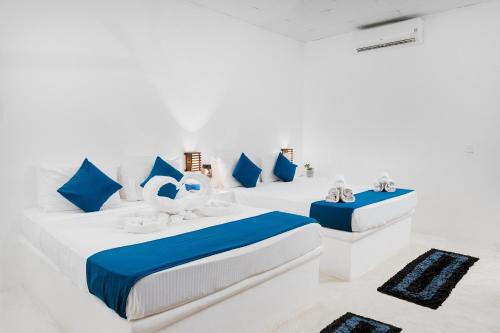 a white room with three beds and blue pillows at Roshanne Beach Resort in Kalpitiya