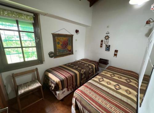 Un dormitorio con dos camas y una silla y una ventana. en La casita en la playa, en Villa Gesell