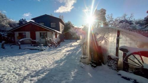 a snow covered yard with a house and the sun at La Loisa - Bungalows & Rooms in San Carlos de Bariloche