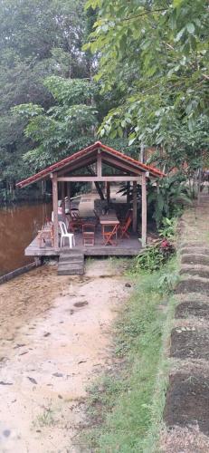 Un pabellón con una mesa y sillas al lado de un río. en Chácara Tauari, en Santo Antônio do Tauá