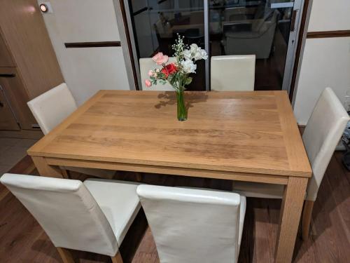 a vase of flowers on a wooden table with white chairs at London Acton Central House in London