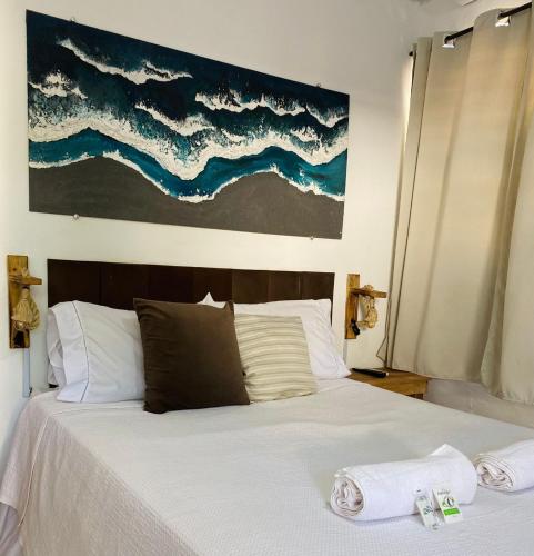 a bedroom with a white bed with a painting on the wall at Encanto Paraty Beach in Paraty