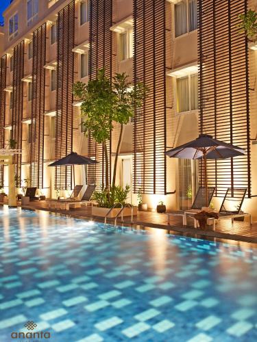 a swimming pool with chairs and umbrellas in front of a building at Ananta Legian Hotel in Legian