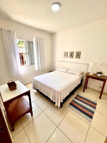 a white bedroom with a bed and a table at Novo Porto- Apartamentos 2 quartos, varanda, cozinha integrada in Piracicaba
