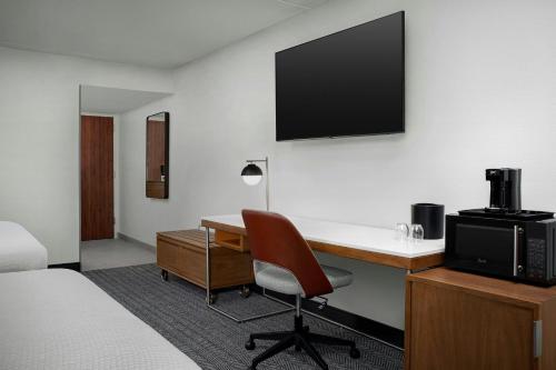 a hotel room with a desk and a tv on the wall at Courtyard by Marriott Bloomington in Bloomington
