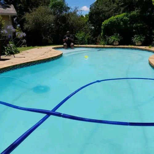 a large blue swimming pool with a man sitting on the curb at Nzima BnB in Estcourt