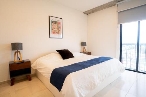 a white bedroom with a bed and a large window at Apartamento Anuva con Parking, Alberca y SkyView in Guadalajara