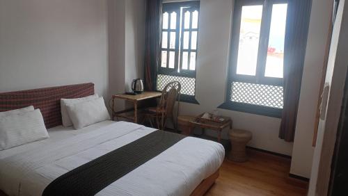 a bedroom with a bed and two windows and a table at Easy Homes - Ashok Stupa in Pātan
