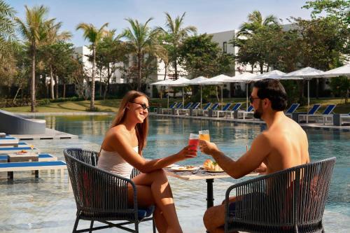 a man and woman sitting at a table by a pool at Hoi An Royal Beachfront Villas in Dien Ban