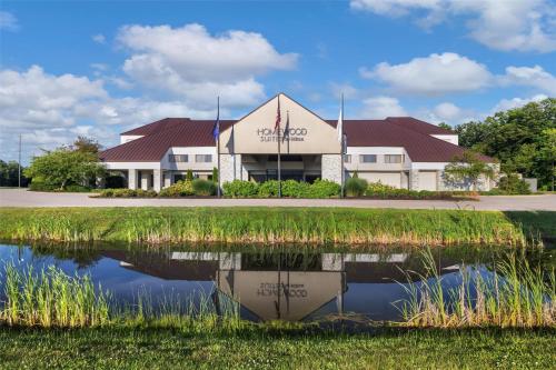 a building with a reflection in a pond at Homewood Suites by Hilton Indianapolis Carmel in Carmel